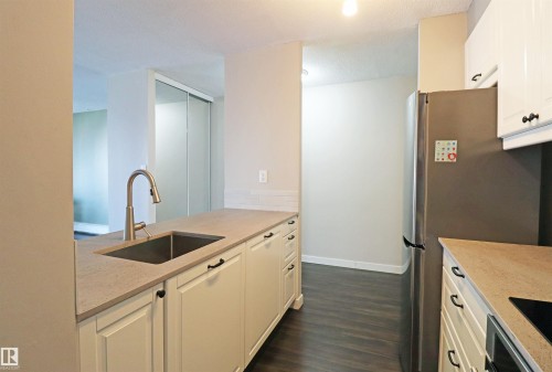 Contemporary kitchen featuring a stainless steel sink with a high-arc faucet, light-toned countertops, white cabinetry with dark hardware, and wood-finish flooring - 901 10160 116 Street, Edmonton, AB - Indoor Photo Showing Kitchen
