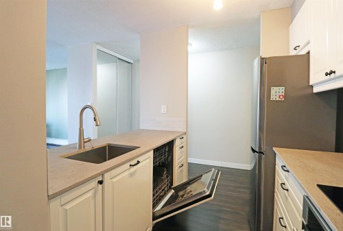 Kitchen featuring light-toned countertops, white cabinetry with dark hardware, stainless steel sink with a pull-down faucet, and a stainless steel refrigerator - 901 10160 116 Street, Edmonton, AB - Indoor Photo Showing Kitchen