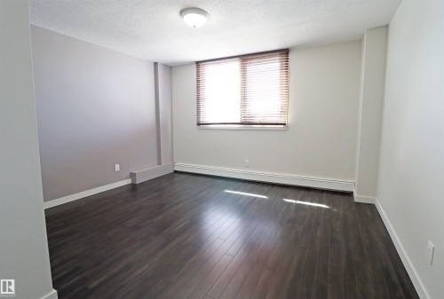 Spacious bedroom featuring dark wood-finish flooring, light-toned walls, and a window with horizontal blinds - 901 10160 116 Street, Edmonton, AB - Indoor Photo Showing Other Room