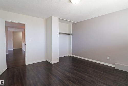 Spacious room featuring dark wood-finish flooring, a neutral accent wall, white baseboards, and an integrated closet with a hanging rod - 901 10160 116 Street, Edmonton, AB - Indoor Photo Showing Other Room