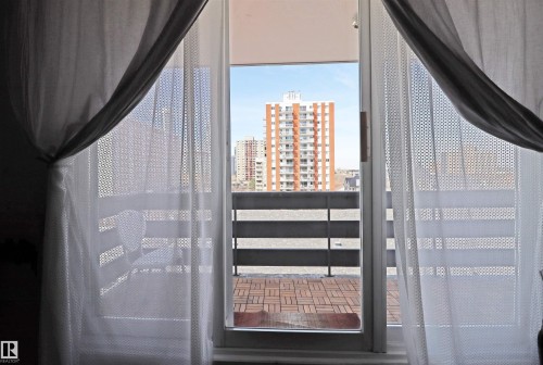 Sliding glass door opening to a private balcony featuring a slatted wood-finish tile floor - 901 10160 116 Street, Edmonton, AB - Indoor Photo Showing Other Room