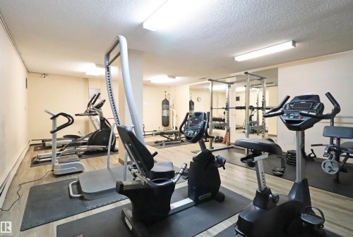Dedicated fitness room featuring wood-finish flooring, fluorescent lighting, and a mirrored wall - 901 10160 116 Street, Edmonton, AB - Indoor Photo Showing Gym Room