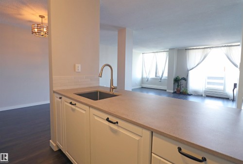 Kitchen counter featuring a stainless steel sink, gooseneck faucet, light-colored countertop, white shaker-style cabinetry with dark hardware, and a subway tile backsplash - 901 10160 116 Street, Edmonton, AB - Indoor Photo Showing Kitchen