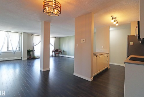 Open-concept living space featuring dark wood-finish flooring, multiple windows with white window treatments, and a decorative ceiling light fixture - 901 10160 116 Street, Edmonton, AB - Indoor