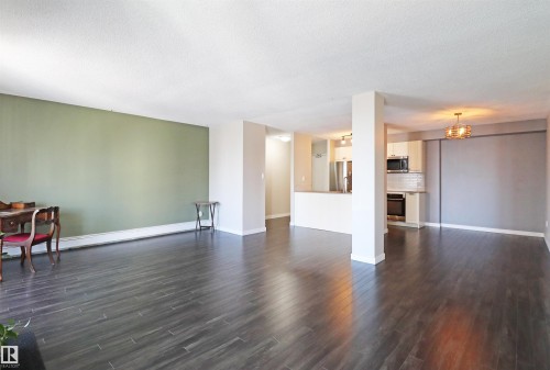 Expansive living area featuring dark wood-finish flooring, a contemporary kitchen with stainless steel appliances, white cabinetry, and a subway tile backsplash - 901 10160 116 Street, Edmonton, AB - Indoor Photo Showing Living Room