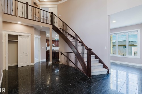 Two-story foyer featuring dark granite-finish flooring, a grand staircase with dark wood banisters and white balusters, and a carpeted second-story landing - 2408 Tegler Green, Edmonton, AB - Indoor Photo Showing Other Room