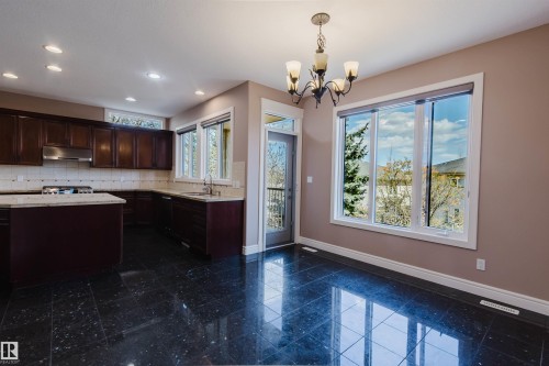 Kitchen and dining area featuring dark wood cabinetry, light-colored countertops, dark tiled flooring, stainless steel range hood, and a chandelier - 2408 Tegler Green, Edmonton, AB - Indoor Photo Showing Kitchen