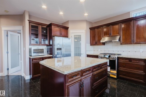 Kitchen featuring dark wood cabinetry, granite countertops, an island with integrated storage, stainless steel appliances, and dark tile flooring - 2408 Tegler Green, Edmonton, AB - Indoor Photo Showing Kitchen