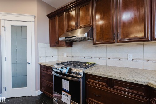 Kitchen featuring wood cabinetry, light-toned stone countertops, and a stainless steel oven range with an overhead hood - 2408 Tegler Green, Edmonton, AB - Indoor Photo Showing Kitchen