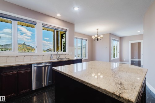Kitchen featuring an expansive island with a light-toned countertop, stainless steel appliances, dark wood cabinetry, and recessed lighting - 2408 Tegler Green, Edmonton, AB - Indoor Photo Showing Kitchen With Double Sink With Upgraded Kitchen