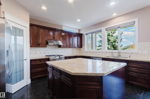 Kitchen featuring a large central island with a light-toned countertop, extensive dark wood cabinetry, a stainless steel range with matching hood, a single basin sink with a gooseneck faucet, and recessed lighting - 2408 Tegler Green, Edmonton, AB - Indoor Photo Showing Kitchen