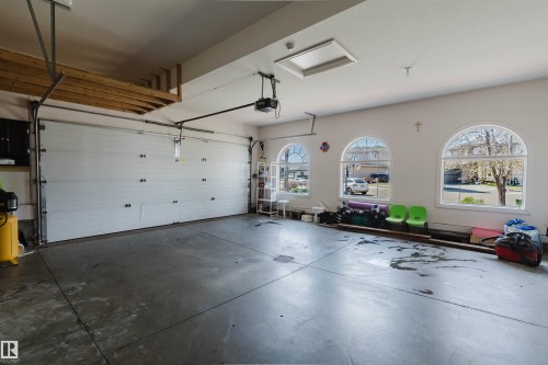 Spacious garage featuring a concrete floor, three arched windows, a white segmented garage door, and an overhead storage rack - 2408 Tegler Green, Edmonton, AB - Indoor Photo Showing Garage