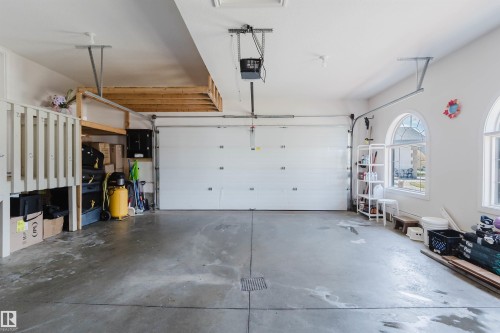 Spacious garage featuring a concrete floor, two arched windows, and a built-in overhead storage platform - 2408 Tegler Green, Edmonton, AB - Indoor Photo Showing Garage