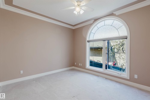 Room featuring a large arched window with decorative upper glass, neutral carpet, light beige walls, and white crown molding - 2408 Tegler Green, Edmonton, AB - Indoor Photo Showing Other Room