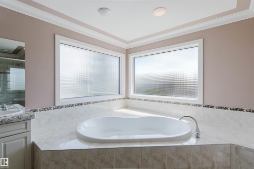 Corner soaking tub with polished chrome fixtures, integrated into a tiled surround featuring a decorative mosaic border - 2408 Tegler Green, Edmonton, AB - Indoor Photo Showing Bathroom