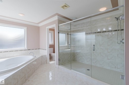 Spacious bathroom featuring a frameless glass shower enclosure with a tiled interior, a built-in soaking tub with a tiled surround, large format polished tile flooring, and a window with privacy glass - 2408 Tegler Green, Edmonton, AB - Indoor Photo Showing Bathroom