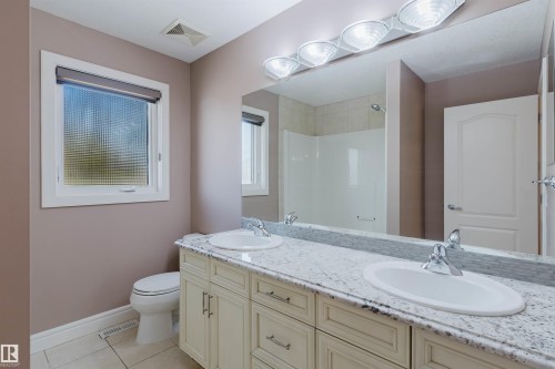 Bathroom featuring a dual vanity with light-toned cabinetry, a speckled countertop, and two undermount sinks with chrome faucets - 2408 Tegler Green, Edmonton, AB - Indoor Photo Showing Bathroom