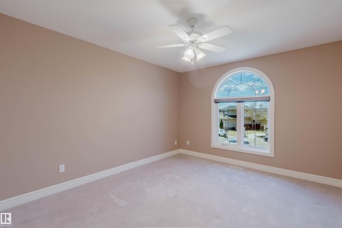 Expansive room featuring neutral wall tones, white trim, light-toned carpeting, an arched window, and a ceiling fan with integrated lighting - 2408 Tegler Green, Edmonton, AB - Indoor Photo Showing Other Room