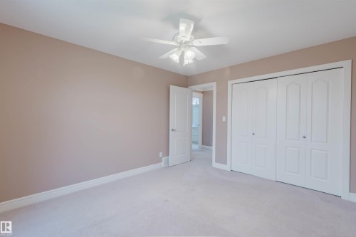 Carpeted room featuring a ceiling fan with integrated lighting, a light tan wall finish, white baseboards, and a bi-fold closet with white panel doors - 2408 Tegler Green, Edmonton, AB - Indoor