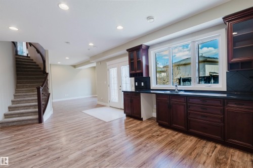 Lower level entertainment area featuring wood-finish flooring, dark wood cabinetry with black countertops, a sink with a window, recessed lighting, and a curved staircase with carpeted treads - 2408 Tegler Green, Edmonton, AB - Indoor Photo Showing Other Room