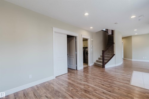 Expansive room featuring wood-finish flooring, recessed lighting, and a curving staircase with dark wood banister - 2408 Tegler Green, Edmonton, AB - Indoor Photo Showing Other Room