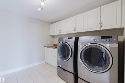 Laundry room featuring track lighting, white upper and lower cabinetry, a stone-finish countertop, and tile flooring - 2408 Tegler Green, Edmonton, AB - Indoor Photo Showing Laundry Room