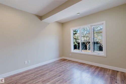 Spacious room featuring a multi-pane window with white trim, wood-finish flooring, light-toned wall paint, white baseboards, and a ceiling beam - 2408 Tegler Green, Edmonton, AB - Indoor Photo Showing Other Room
