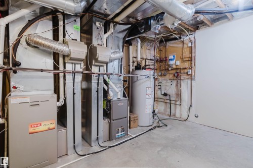 Utility space featuring a Bryant Plus 90x furnace, a secondary furnace unit, a water heater, exposed copper piping, and an unfinished concrete floor - 2408 Tegler Green, Edmonton, AB - Indoor Photo Showing Basement