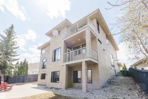 Three-story stucco exterior featuring two balconies with white railings, multiple windows including an arched design, and a lower-level patio with pavers - 2408 Tegler Green, Edmonton, AB - Outdoor With Balcony