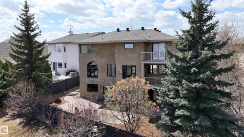 Multi-level stone facade residence featuring a lower-level patio, two upper-level balconies with metal railings, and a prominent arched window design - 2408 Tegler Green, Edmonton, AB - Outdoor
