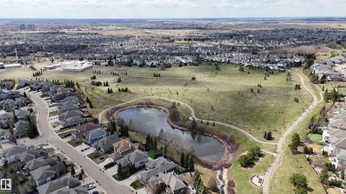 Aerial perspective of a residential community featuring a prominent central pond, extensive green spaces, and paved walking paths - 2408 Tegler Green, Edmonton, AB - Outdoor With View