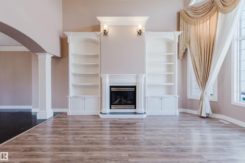 Central fireplace flanked by built-in shelving and cabinetry, wood-finish flooring, and arched entryway - 2408 Tegler Green, Edmonton, AB - Indoor With Fireplace