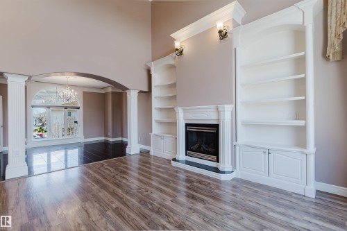 Living area featuring wood-finish flooring, a fireplace with a white mantel, and built-in shelving - 2408 Tegler Green, Edmonton, AB - Indoor With Fireplace