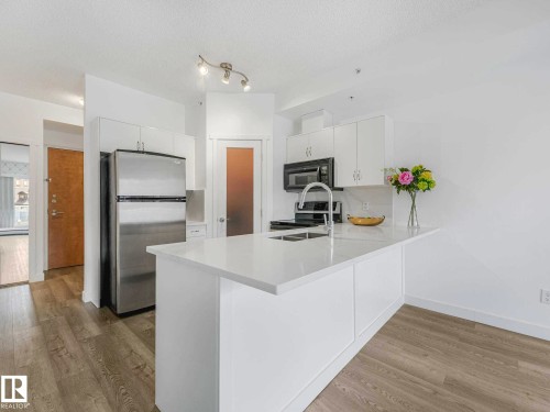Kitchen featuring white cabinetry, stainless steel appliances, a center island with an integrated sink, and wood-finish flooring - 305 10504 99 Avenue, Edmonton, AB - Indoor Photo Showing Kitchen With Double Sink With Upgraded Kitchen