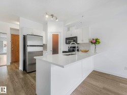Kitchen featuring white cabinetry, stainless steel appliances, a center island with an integrated sink, and wood-finish flooring - 