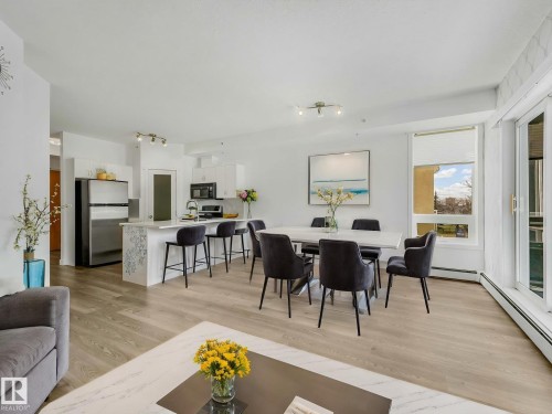 Open-concept living space featuring wood-finish flooring, a contemporary kitchen with a breakfast bar, a dedicated dining area, and large windows with natural light - 305 10504 99 Avenue, Edmonton, AB - Indoor