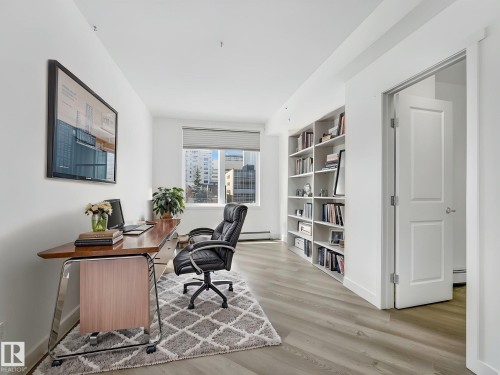 Dedicated workspace featuring light wood-finish flooring, a built-in white shelving unit, a window with roller shades, and a white two-panel door - 305 10504 99 Avenue, Edmonton, AB - Indoor