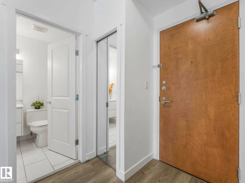 Entryway featuring a natural wood-finish door with silver-tone hardware, wood-finish flooring, and a mirrored closet door - 305 10504 99 Avenue, Edmonton, AB - Indoor Photo Showing Bathroom