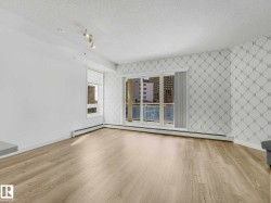 Living area featuring wood-finish flooring, a patterned accent wall, track lighting, and a balcony with cityscape scenery - 
