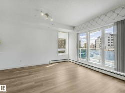 Bright living area featuring wood-finish flooring, white painted walls, a large window with a roller shade, and a three-panel glass sliding door leading to an exterior balcony - 