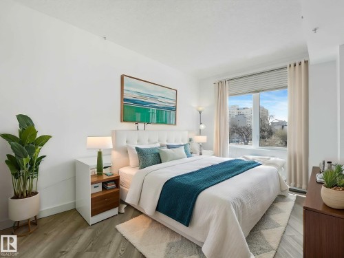 Bedroom featuring a large window, light wood-finish flooring, white walls, a white upholstered headboard, and a built-in wood and white side table - 305 10504 99 Avenue, Edmonton, AB - Indoor Photo Showing Bedroom
