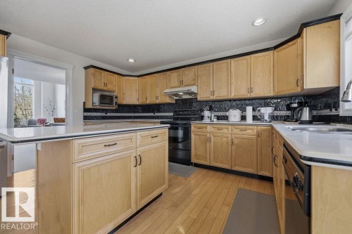 Kitchen featuring wood-finish flooring, light wood cabinetry with dark trim, dark patterned backsplash, light countertops, and a central island with countertop seating - 11551 14 Avenue, Edmonton, AB - Indoor Photo Showing Kitchen With Double Sink