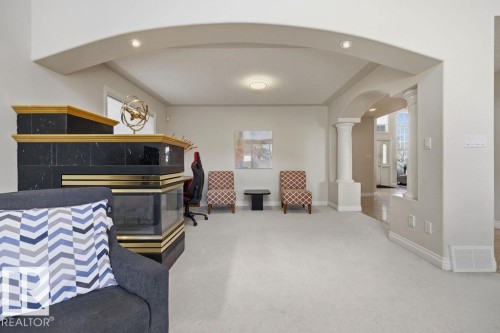 Spacious interior featuring a prominent black and gold fireplace, arched doorways, white columns, recessed lighting, and light-colored carpet flooring - 11551 14 Avenue, Edmonton, AB - Indoor