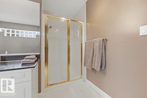 Shower enclosure with gold-tone framing, white tile flooring, and a vanity with a dark countertop and white cabinetry - 11551 14 Avenue, Edmonton, AB - Indoor Photo Showing Bathroom