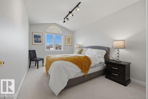 Bedroom featuring a large arched window with clear glass, light-colored carpeting, white baseboards, and a track lighting fixture on the vaulted ceiling - 11551 14 Avenue, Edmonton, AB - Indoor Photo Showing Bedroom