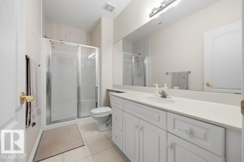 Bathroom featuring a white vanity with integrated sink, a large wall-mounted mirror, a glass-enclosed shower with tiled surround, and ceramic tile flooring - 11551 14 Avenue, Edmonton, AB - Indoor Photo Showing Bathroom