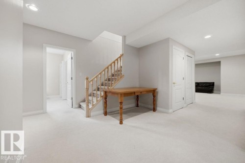 Finished basement area featuring plush light-toned carpeting, recessed ceiling lighting, a wood-finish staircase with balusters, and white paneled doors - 11551 14 Avenue, Edmonton, AB - Indoor Photo Showing Other Room