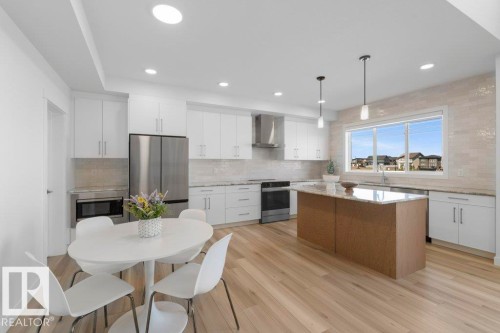 Modern kitchen featuring white cabinetry, stainless steel appliances, a center island with pendant lighting, and light wood-finish flooring - 19110 20A Avenue, Edmonton, AB - Indoor