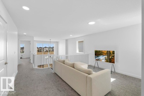 Open concept loft space featuring light gray carpeting, white walls, recessed lighting, white railing with vertical balusters, and a large window offering natural light - 19110 20A Avenue, Edmonton, AB - Indoor