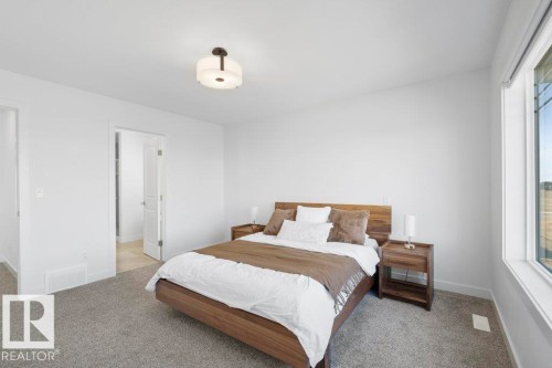 Carpeted bedroom featuring a large window with white trim, a flush-mount ceiling light fixture, and a white interior door - 19110 20A Avenue, Edmonton, AB - Indoor Photo Showing Bedroom